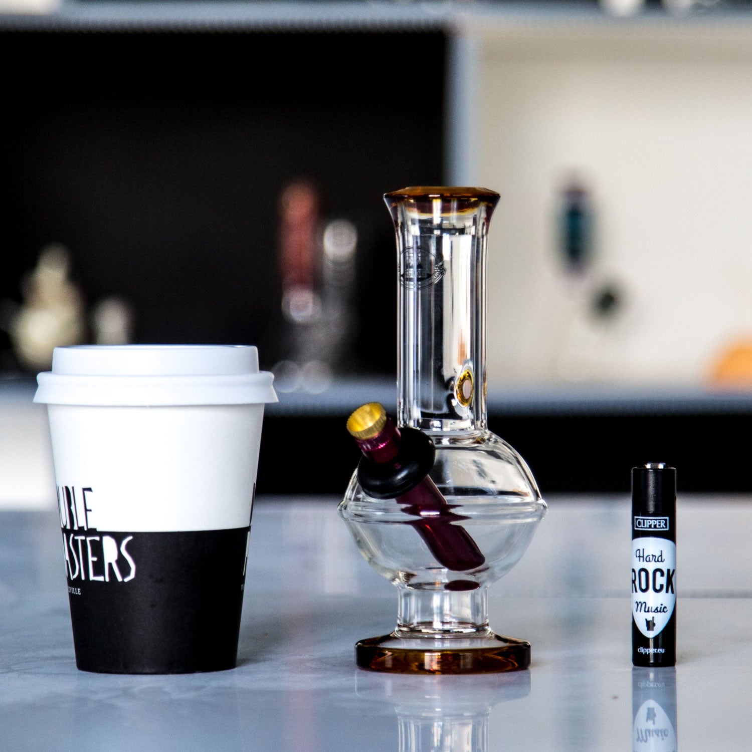 Small Aussie Agung glass bong on a table with lighter and coffee cup for size comparison.